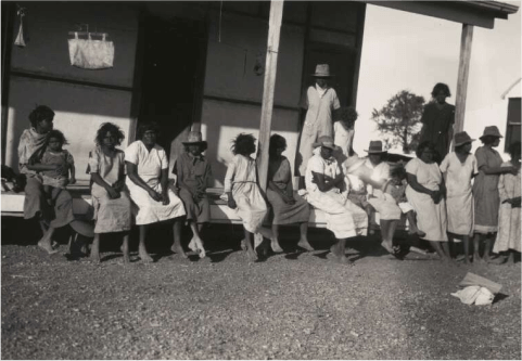 A black and white photo of Aboriginal women and children sitting on a verandah at Brunette Downs Station, Northern Territory, 1930