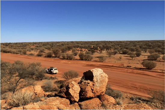 A color photo of a car driving on a dirt road
