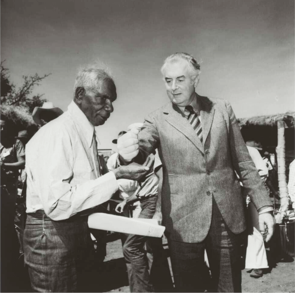 A black and white photo of Prime minister Gough Whitlam pours soil into the hand of Gurindji Traditional Land Owner Vincent Lingiari at Wattie Creek, Northern Territory, 16 August 1975. Source: National Library of Australia